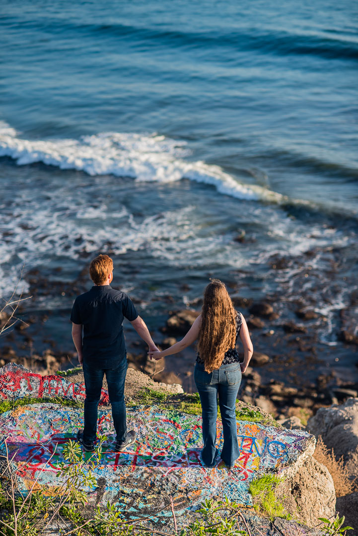 Couple holding hands above a colorful coastal overlook