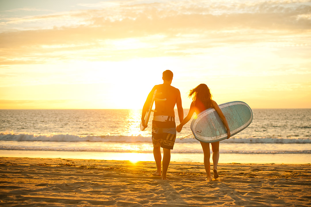 Couple walking toward the ocean at sunset with surfboards
