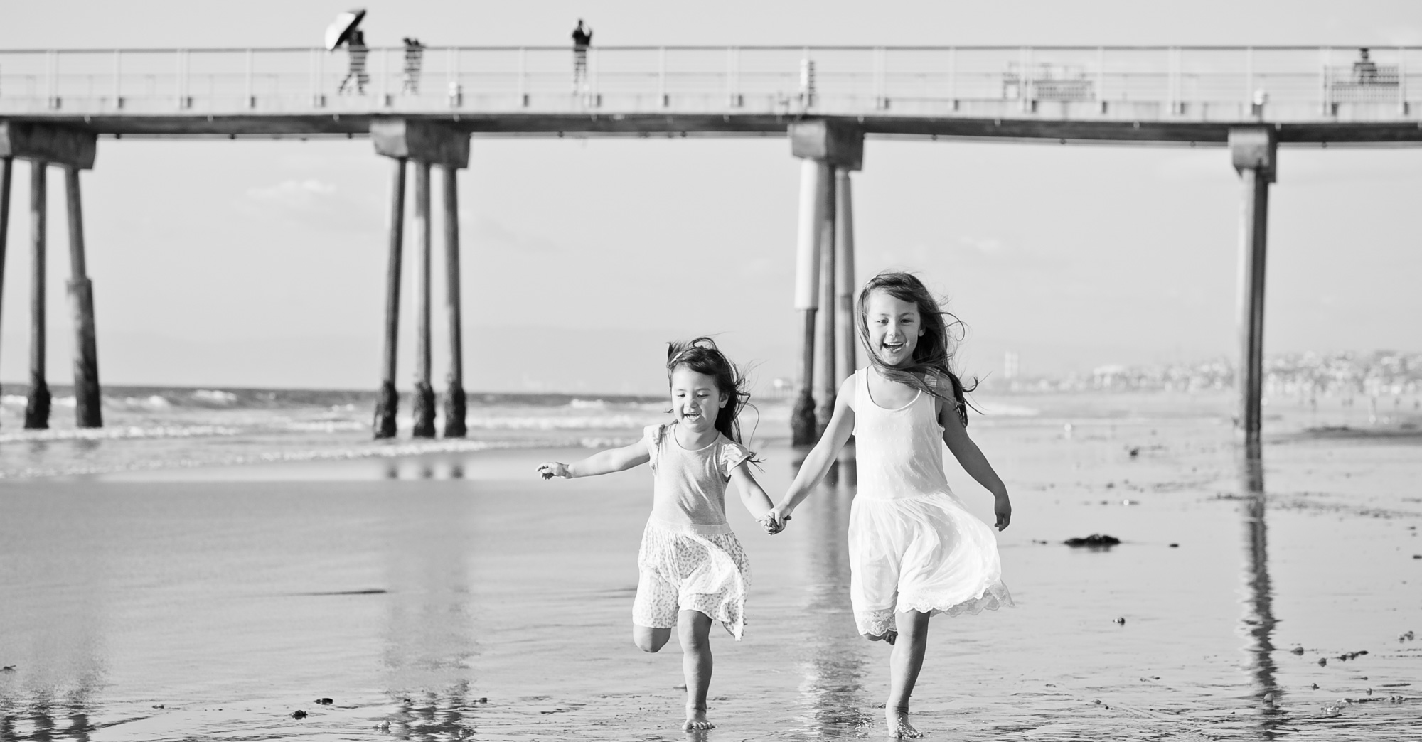 Two sisters running hand in hand beneath the Hermosa Beach Pier