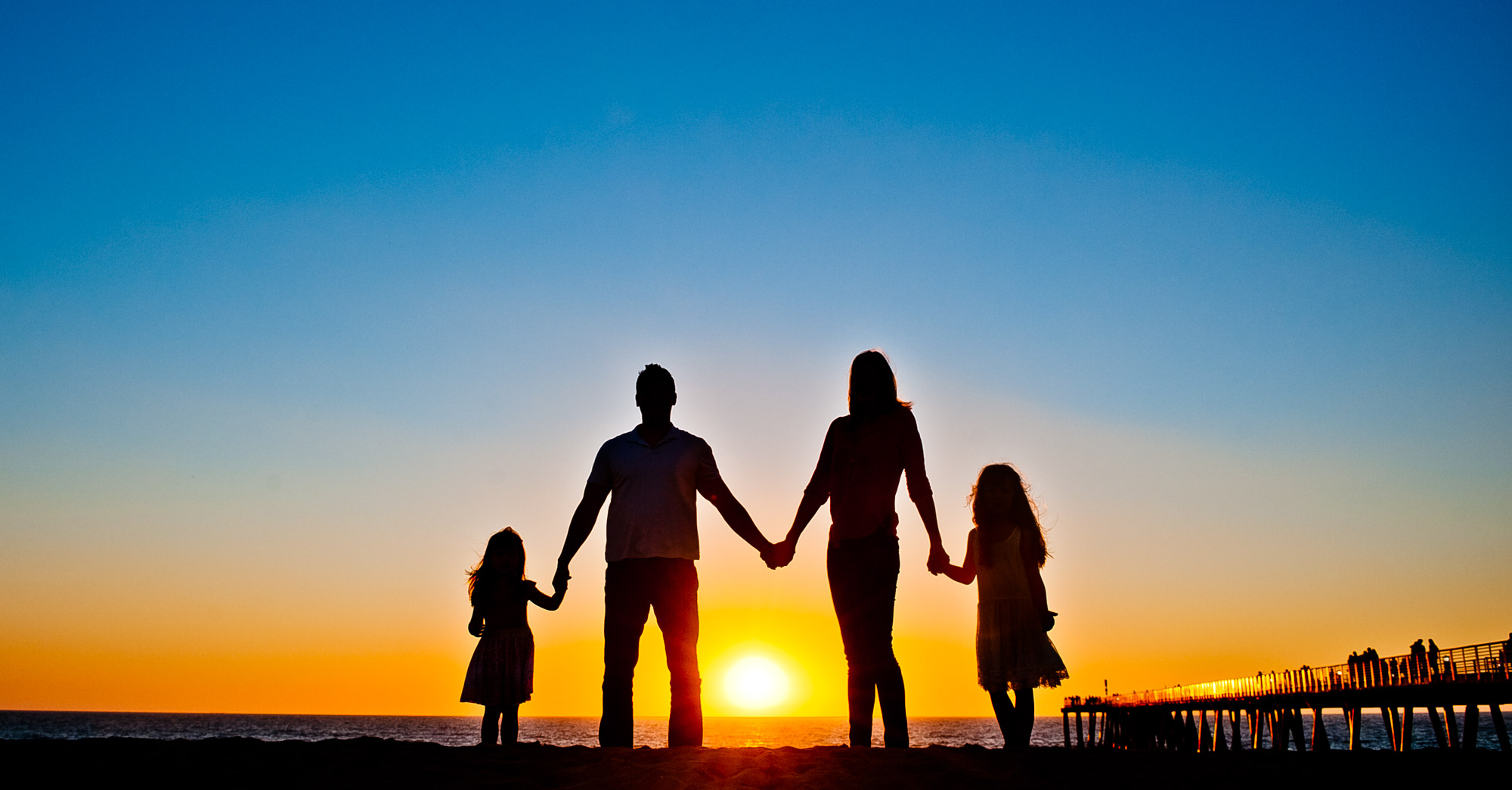 Family of four holding hands in silhouette at a Hermosa Beach sunset